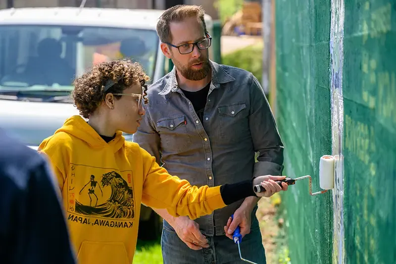卡尔森 assisting a student paint a wall with a paint roller.